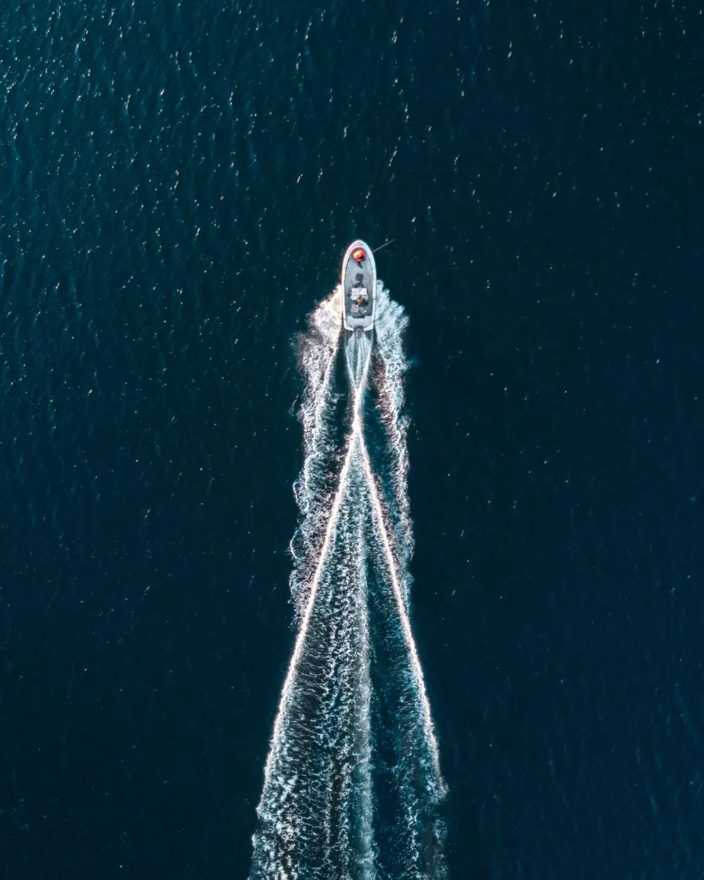 A motorboat seen from directly above, cutting a wake across deep blue water.